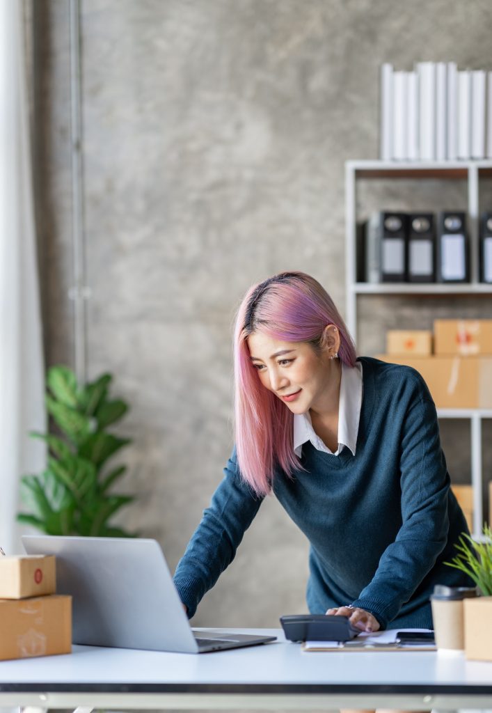 Portrait of a young Asian businesswoman sitting at a desk in an office recording data on a laptop. f