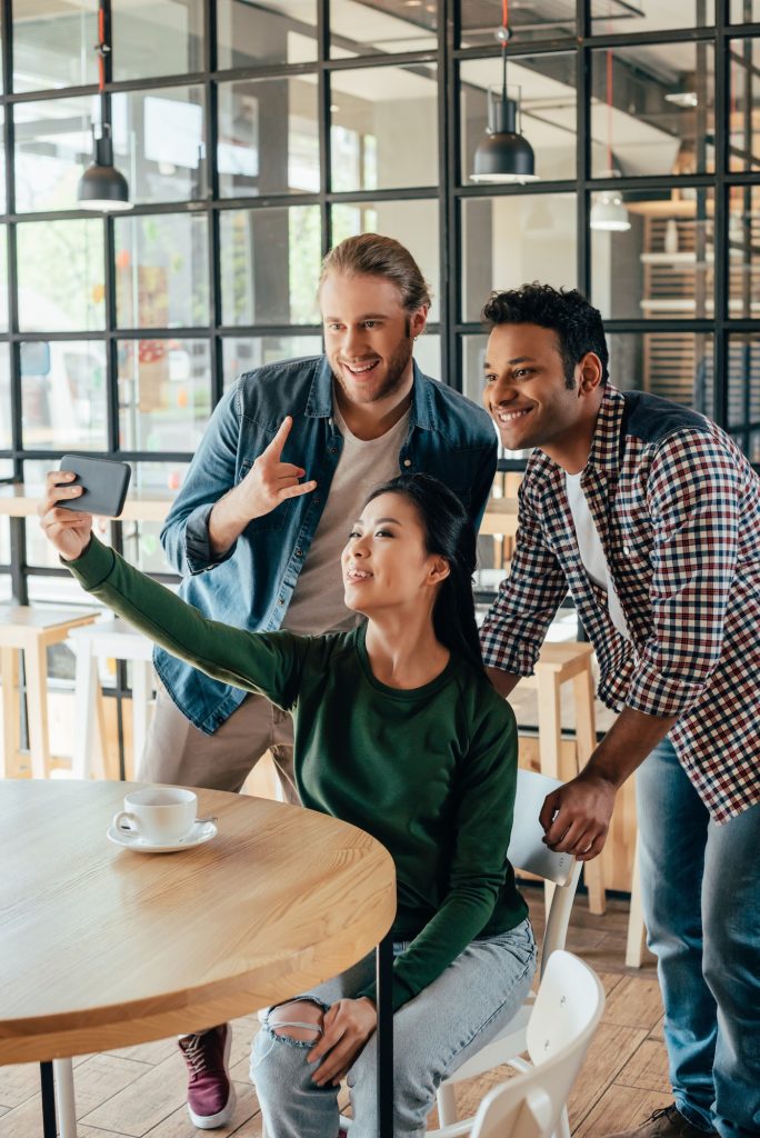 Young happy multiethnic friends taking selfie in cafe